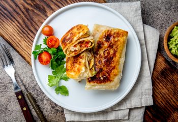 Mexican chimichanga on white plate served with guacamole sauce. Fried tortilla stuffed with chicken and vegetables. Traditional Mexican food, Top view